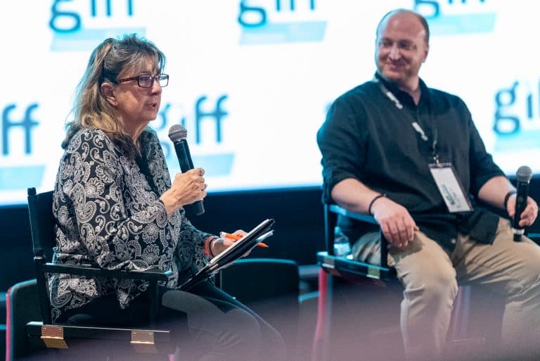 GIFF 2026 panel moderator speaking into a microphone next to a panelist on stage, with the festival logo backdrop behind them.