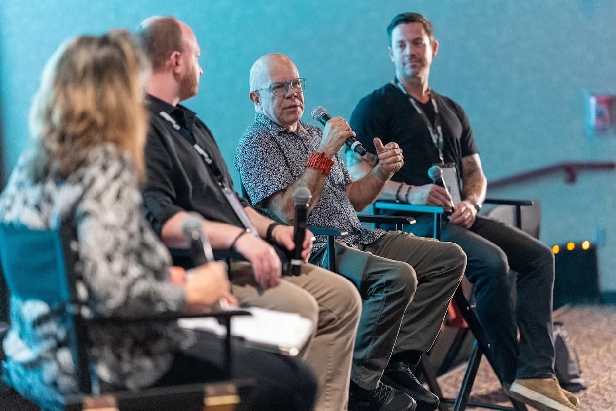 AI in Filmmaking panel at the Gasparilla International Film Festival 2026, three panelists seated on stage in director chairs, one speaking into a microphone, with the moderator in the foreground.