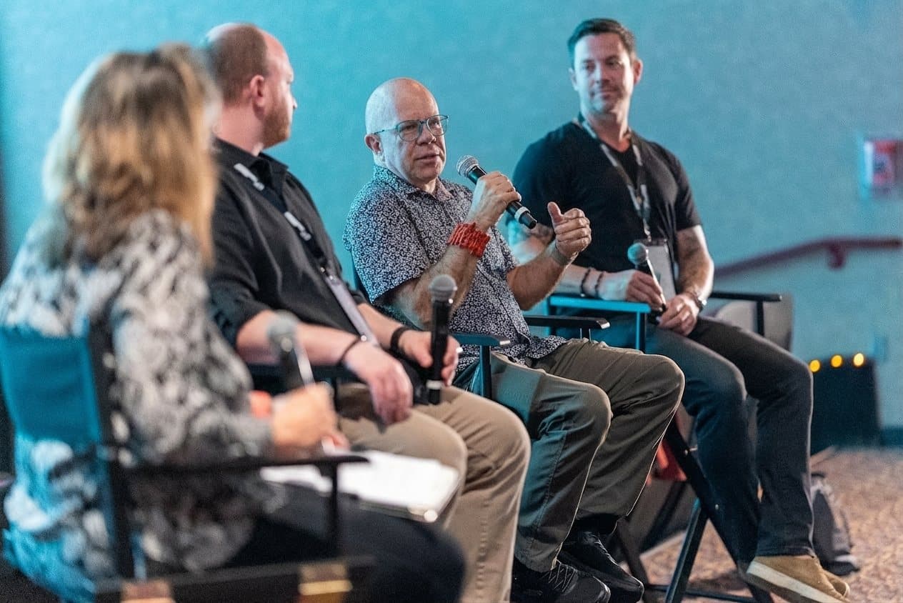 AI in Filmmaking panel at the Gasparilla International Film Festival 2026, three panelists seated on stage in director chairs, one speaking into a microphone, with the moderator in the foreground.